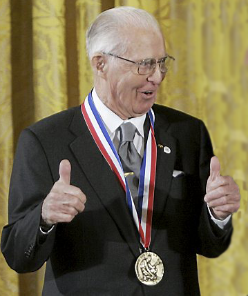 Norman receives the Nobel Prize in a black suit, gray tie white hair and glasses.